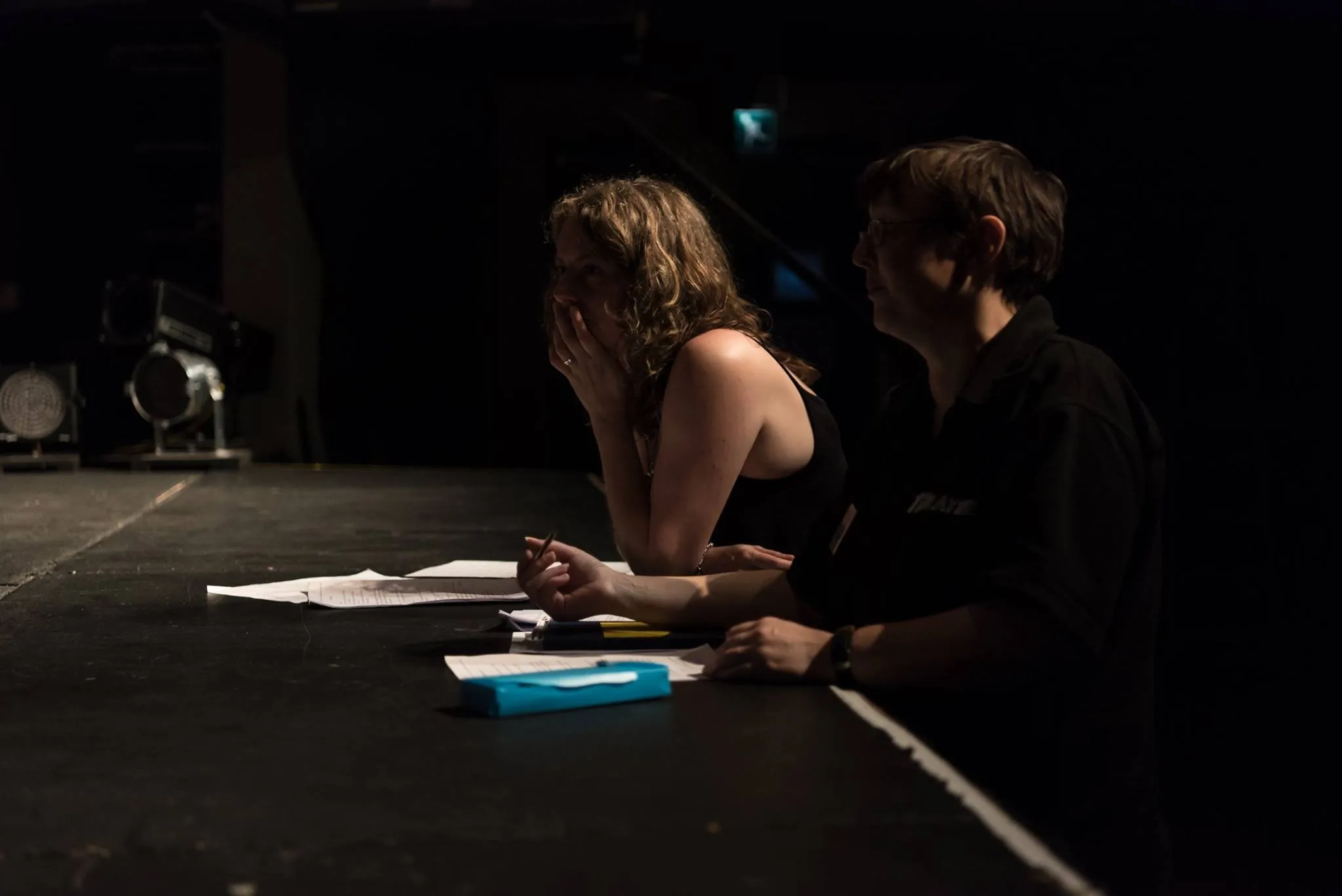 Two production team members at a stage-edge desk reviewing notes during a rehearsal