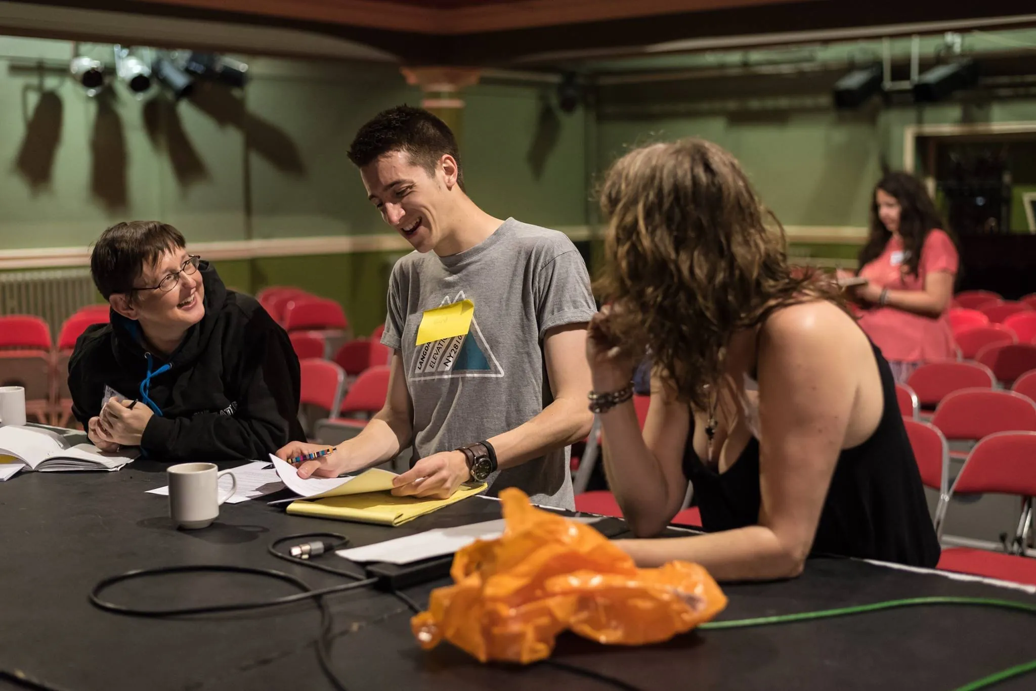 Production team sharing a joke at a table on stage during rehearsals in a small theatre
