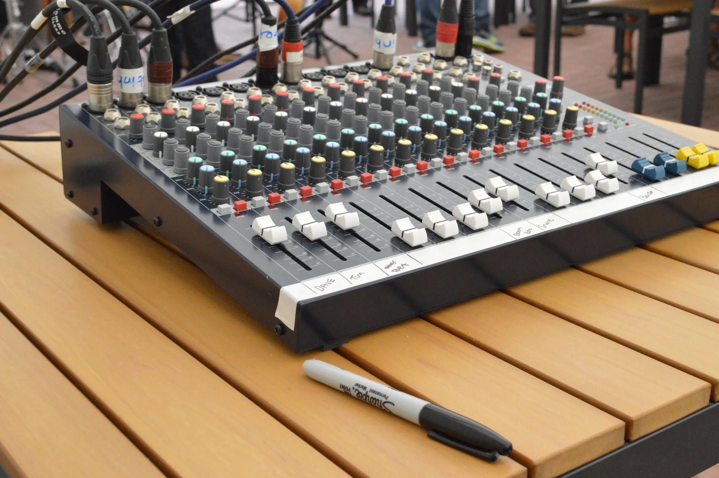 Compact analogue mixing desk with labelled channels and XLR cables set up on an outdoor table