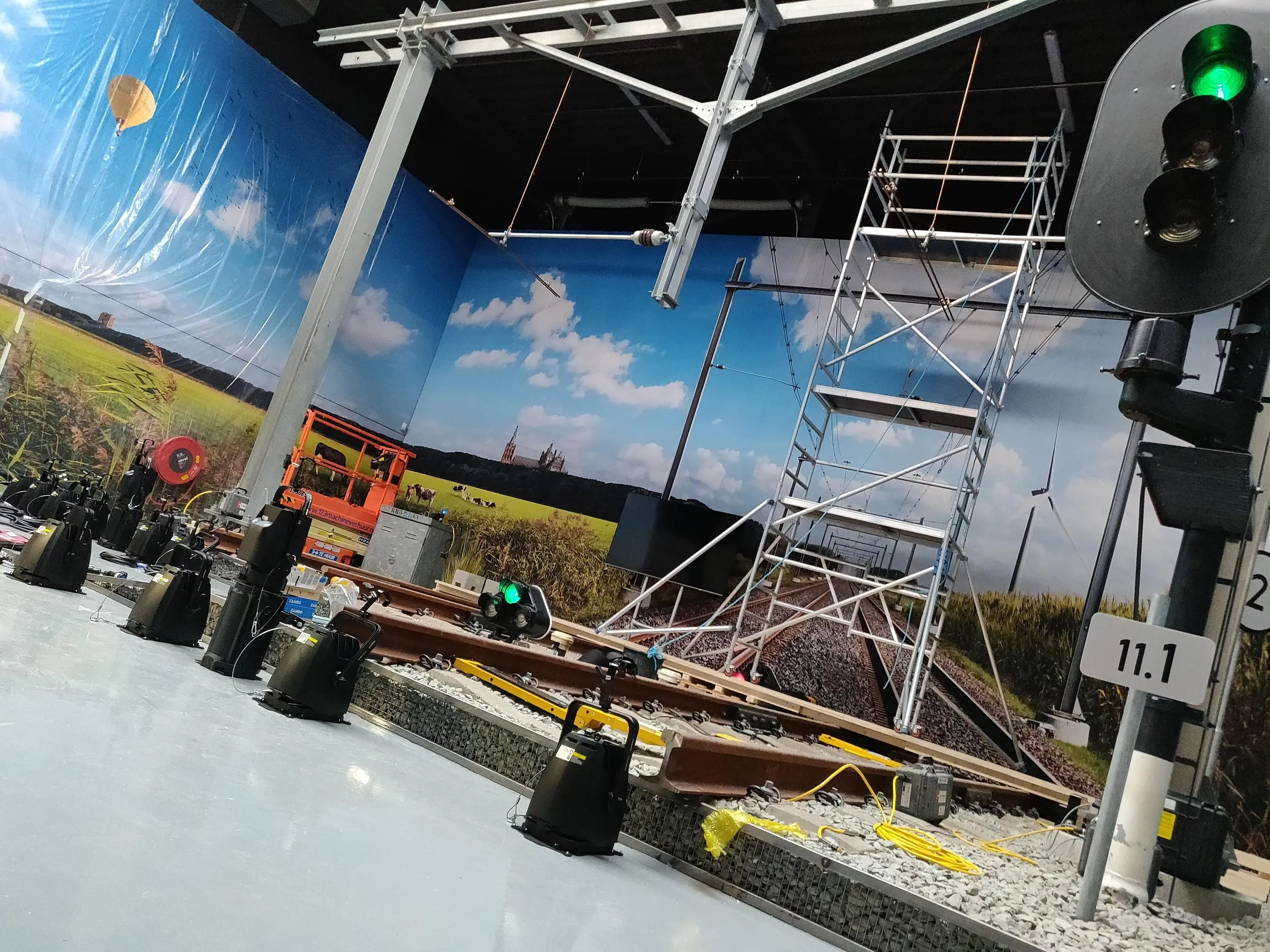 Indoor demo railway with track, signal and scaffold tower against a countryside mural during installation