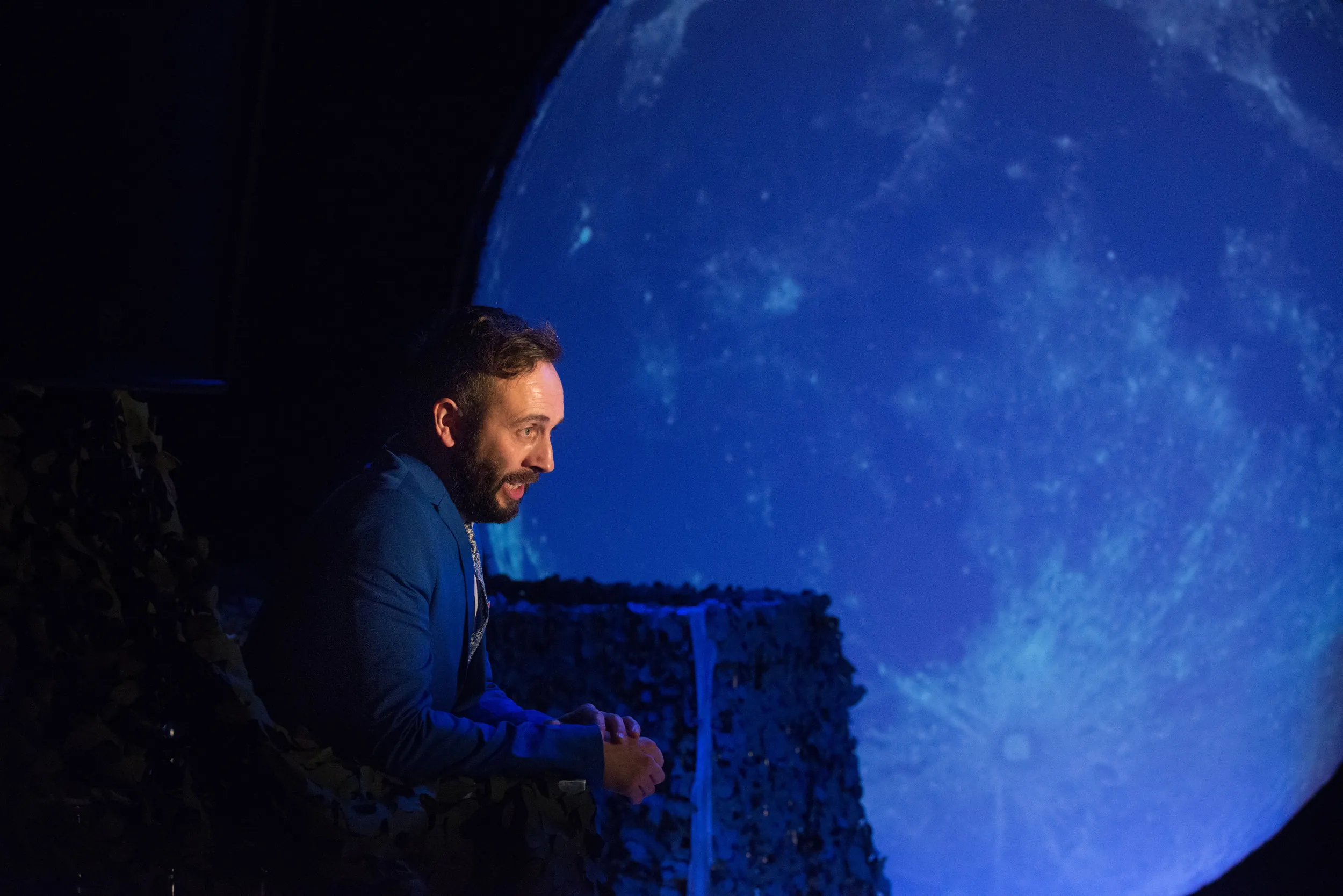 Actor in a blue suit performing in front of a huge glowing full-moon backdrop
