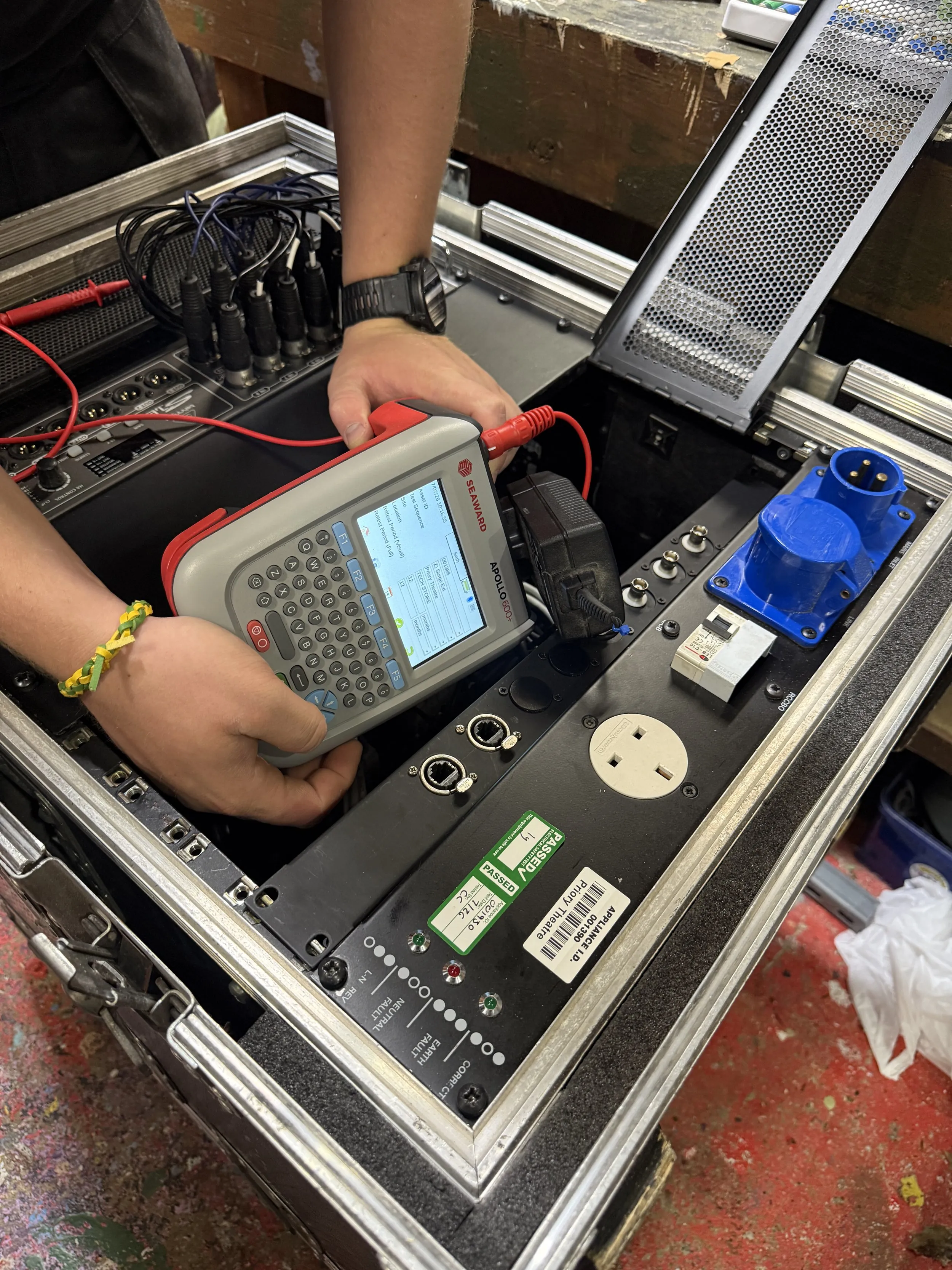 Technician PAT testing a power distribution unit in a flight case with a handheld Seaward Apollo tester